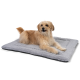 Ein flauschiger, tanfarbener Hund liegt auf einem weichen grauen Haustierbett mit einer strukturierten Oberfläche und schaut verspielt in die Kamera.