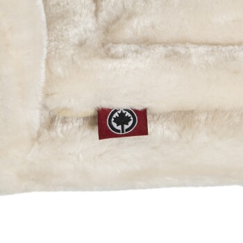 Nahaufnahme einer weichen, cremefarbenen Haustierdecke mit einem roten Etikett mit einem schwarzen Baumlogo, das die Markenqualität anzeigt.