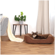 Ein kleiner brauner Hund ruht sich in einem gemütlichen braunen Haustierbett aus, mit einer Topfpflanze und einem grauen Sofa in einem hellen, modernen Wohnzimmer.