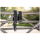 Zwei schwarze Haustiergeschirre mit Metallringen und Schnallen, die an einem Holzzaun in einer natürlichen Umgebung hängen.