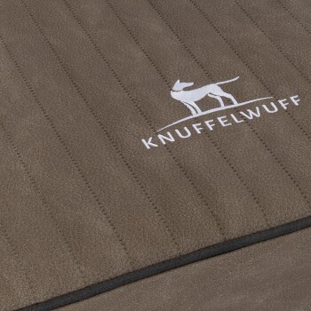 Eine Nahaufnahme eines braunen Haustierbettes mit vertikaler Naht und dem gestickten Logo 'KNUFFELWUFF' mit einer Silhouette eines Hundes.