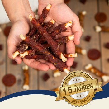 Hände halten Hundekau-Sticks mit verstreuten Leckereien im Hintergrund; ein Abzeichen liest "Beste Qualität" und "15 Jahre."