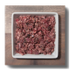Ein quadratisches weißes Geschirr gefüllt mit fein gehacktem rohem Fleisch, auf einer Holzoberfläche platziert.