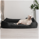 Ein weißer Hund liegt auf einem plüschigen, dunkelgrauen Haustierbett in einem modernen Raum mit einer dekorativen Lampe und einer Topfpflanze im Hintergrund.
