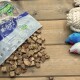 Verschüttete Tüte mit würfelförmigen Hundeleckerlis auf einem Holztisch neben einem Tau-Knoten und zwei Plüschmäusen; Verpackung mit der Aufschrift 'NATURE POWER'.