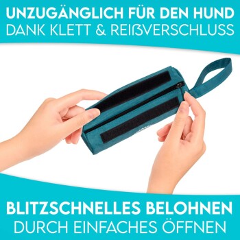 Eine Person hält eine türkisfarbene Hundeleckerlitasche mit Klettverschluss und Reißverschluss, mit den Aufschriften "UNZUGÄNGLICH FÜR DEN HUND" und "BLITZSCHNELLES BELOHNEN".