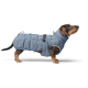 Ein Dackel, der einen hellblauen, gepolsterten Hundemantel trägt, steht vor einem weißen Hintergrund und zeigt sein stilvolles und warmes Design.