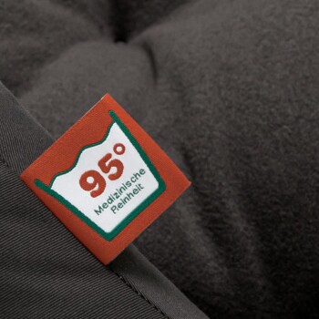 Nahaufnahme eines Haustierbettes mit einem Etikett, das "95° Medizinische Reinheit" liest, was medizinische Sauberkeit anzeigt, vor einem dunklen Stoffhintergrund.