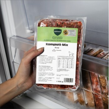 Hand hält vakuumverpackte 'Komplett‑Mix Rind' Barfer's Complete 500‑g Hundefutterpackung im Gefrierschrank.