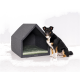 Ein schwarz-brauner Hund sitzt neben einem modernen, grauen Hundehäuschen mit einem grünen Kissen innen, vor einem weißen Hintergrund.