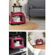 Weiße Katze ruht in einer rosa, weichwandigen Tragetasche mit Netz auf einem runden Jute‑Teppich neben einem grauen Sofa.