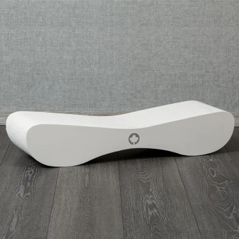 Ein schlankes, modernes weißes Hundebett mit wellenförmigem Design, auf dunklem Holzboden vor einem grauen Hintergrund platziert.