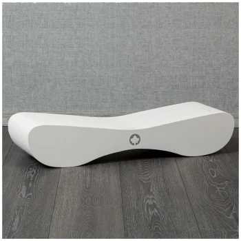Ein schlankes, modernes weißes Hundebett mit wellenförmigem Design, auf dunklem Holzboden vor einem grauen Hintergrund platziert.