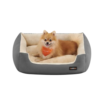 Ein flauschiger Pomeranian-Hund mit einem orangefarbenen Halstuch entspannt sich in einem gemütlichen grauen Haustierbett mit einem weichen cremefarbenen Innenraum.