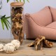 Ein Glasbehälter voller natürlicher Hundekauartikel steht auf einem Holztisch neben einem plüschigen rosa Haustierbett und einem weißen Seilspielzeug.