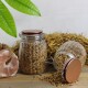 Zwei Gläser mit Kupferdeckeln gefüllt mit Vogelfutter, eines gekippt und auf Holz verschüttet; Heuhintergrund und Leckstein.