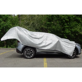 Schattennetz 2x3m Ein silbernes Auto, das mit einer glänzenden, reflektierenden Plane bedeckt ist, parkt auf einer Straße, die von Grün umgeben ist.