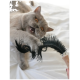 Eine verspielte graue Katze mit orangefarbenen Augen greift nach einem schwarzen Feder-Spielzeug, das von einer Hand gehalten wird, und zeigt Aufregung und Engagement.