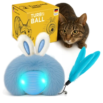 Ein blauer, flauschiger Spielzeug, das einem Hasen ähnelt, mit leuchtenden Augen und angehängten Federn, neben einer gelben Box mit der Aufschrift "Turbo Ball", entwickelt in Deutschland.