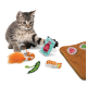 Un chaton tabby gris joueur atteint un paquet de "KONG Sauce Soja" parmi des jouets en peluche colorés sur un tapis marron illustré de nourriture.
