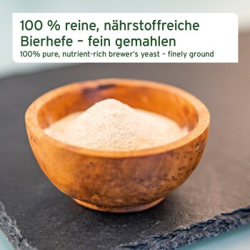 Eine Holzschale, gefüllt mit einem hellbraunen Pulver, steht auf einer dunklen Schieferoberfläche. Der Text lautet 'Mit wichtigen Nährstoffen' und 'Ohne synthetische Zusätze.'