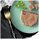 Une tranche de pâté pour animaux de compagnie sur une assiette vert clair, accompagnée de petits cubes du même pâté et d'une branche de persil, avec une fourchette dorée à proximité.