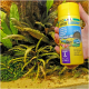 Een hand die een gele container Pro Novo Shrimps visvoer vasthoudt, met tekst in meerdere talen, omringd door waterplanten.