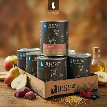 Stapel LIEBESGUT Hundefutterdosen in Markenschale mit Birnen, rohem Fleisch, Beeren und Öl; sichtbarer Text ‚LIEBESGUT – WEIL LIEBE GUT TUT‘ und ‚Für Hunde‘.