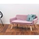 Ein stilvolles pinkes Haustiersofa mit Holzbeinen, ausgestattet mit zwei hellblauen Kissen, auf einem Holzboden vor einer schlichten Wand.