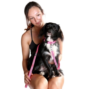 Eine Frau hält einen kleinen schwarz-weißen Hund mit einem rosa Halsband und Leine, der ein stilvolles Haustierzubehör präsentiert.