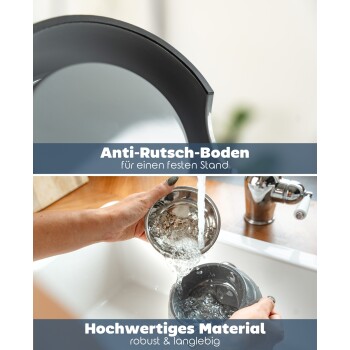 Eine Person gießt Wasser aus einer Edelstahlschüssel in einen grauen Haustier-Wasserbrunnen, mit einer modernen Küchenspüle und einem Wasserhahn im Hintergrund.