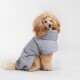 Ein flauschiger Hund trägt einen gemütlichen grauen Haustiermantel und sitzt vor einem schlichten weißen Hintergrund.
