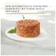 Haustierfutter auf einem weißen Teller mit zerkleinertem Fleisch, Sauce und einem Basilikumblatt. Deutscher Text: "Fein geschnetzelte Stückchen mit Sauce."