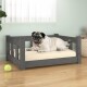 Ein entspannter Mops liegt auf einem grauen Holzhaustierbett mit einem beigen Kissen, neben einem grünen Tennisball auf einem Holzboden.