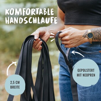 Eine Frau hält eine schwarze Hundeleine mit einem bequemen Griff, beschriftet mit "Komfortable Handschlaufe" und "Gepolstert mit Neopren."