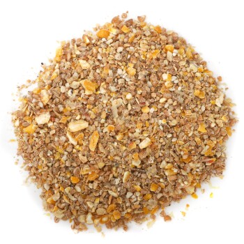 Nahaufnahme eines Haufens Haustierfutterkörner, die eine Mischung aus braunen und orangefarbenen Stückchen auf einem weißen Hintergrund zeigt.