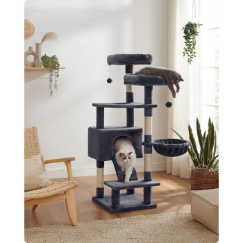 Ein grauer Katzenbaum mit mehreren Ebenen, einem gemütlichen Versteck und hängenden Spielzeugen, in einem hellen Raum mit Pflanzen und einem Stuhl.