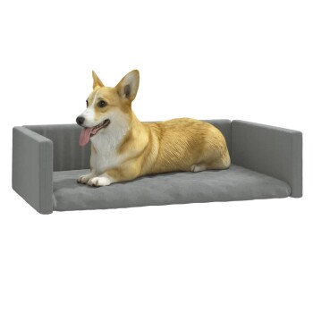 Ein entspannter Corgi, der auf einem grauen Haustierbett mit erhöhten Seiten liegt, zeigt seinen verspielten Ausdruck und die Zunge heraus.