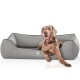 Ein glücklicher brauner Hund, der auf einem grauen Hundebett mit einem Logo, das "KNUFFELWUFF" liest, entspannt und Komfort sowie Stil zeigt.