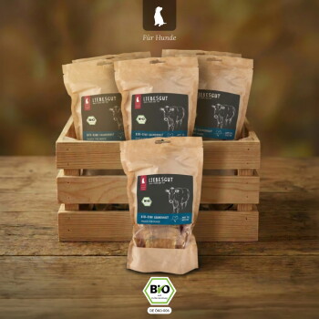 Braune Papiertüten mit Liebesgut Bio-Hundesnacks mit Kuhlogo und BIO-Siegel in Holzkiste, Kopfzeile 'Für Hunde' sichtbar.