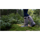 Nahaufnahme der Beine einer Person in grauen wasserdichten Stiefeln, die auf moosigem Boden stehen, umgeben von üppigen grünen Farnen in einem Wald.