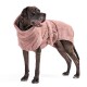 Ein schwarz gestromter Hund, der einen weichen, rosa, kapuzenartigen Handtuch-Roben trägt, steht vor einem weißen Hintergrund und sieht zufrieden aus.