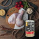 Rohe Hähnchenkeulen auf einem Holzbrett mit Tomaten und Kräutern sowie einer Dose Liebesgut Katzenfutter mit der Aufschrift „BIO‑GANS FÜR KATZEN“.