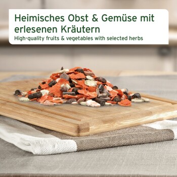 Gemischte Trockenfrüchte, Gemüseflocken und Pellets auf einem Holzbrett; Etikett auf Deutsch und Englisch: 'Früchte & Gemüse'.