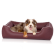 Ein glücklicher Australian Shepherd Hund, der in einem burgunderfarbenen Haustierbett mit weißem Rand entspannt, mit einem Holzschild, das 'KNUDDELWUFF' beschriftet ist.