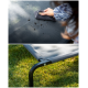 Eine Person, die ein graues Haustierbett mit einem Tuch reinigt, das Schmutz auf dem Stoff zeigt, mit einer Nahaufnahme des stabilen Metallrahmens des Bettes auf Gras.