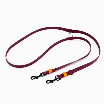 Nahaufnahme einer burgunderfarbenen Haustierleine mit einem schwarzen Metallring und zwei schwarzen Druckknöpfen, vor einem weißen Hintergrund.