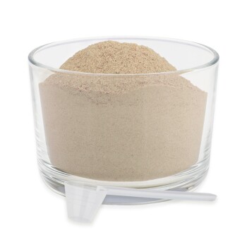 Ein Glasbehälter gefüllt mit hellbraunem Pulver, begleitet von einem kleinen weißen Löffel, der an der Seite liegt.