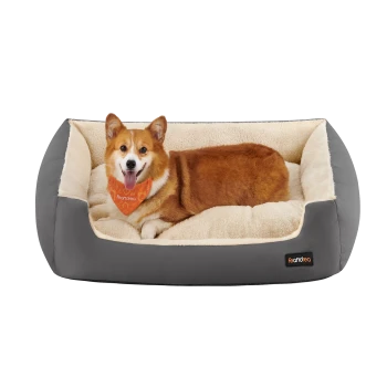 Ein glücklicher Corgi mit einem orangefarbenen Halstuch ruht sich bequem in einem plüschigen, grauen Hundebett mit einem weichen cremefarbenen Innenraum aus.