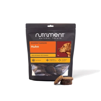 Schwarze Tüte von Nutriment Natural Treats Gourmet-Burgers ‚Huhn‘ 1 kg mit Hundefoto und gestapelten runden Hähnchen-Trainingsleckerli.